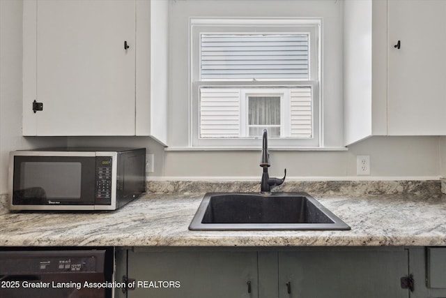 kitchen featuring a sink, light countertops, white cabinets, black dishwasher, and stainless steel microwave