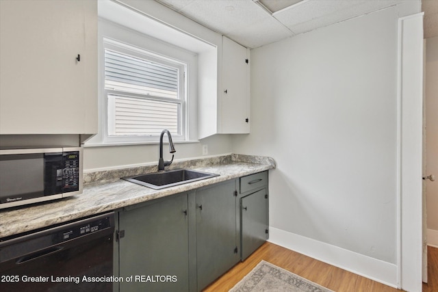 kitchen featuring baseboards, a drop ceiling, dishwasher, light wood-style floors, and a sink