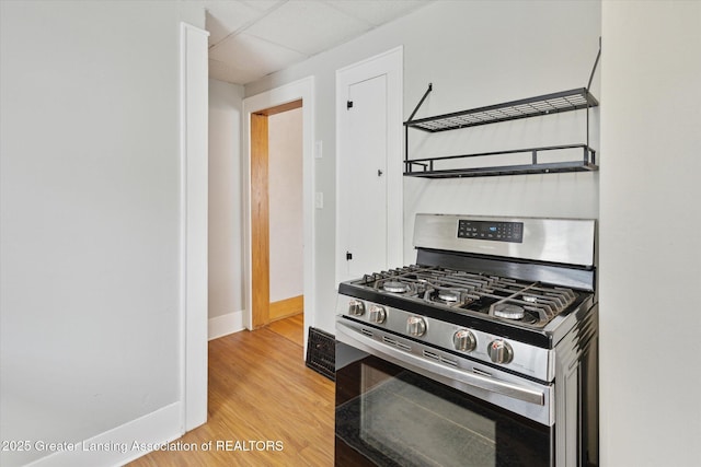 kitchen with light wood-style flooring, a drop ceiling, baseboards, and stainless steel range with gas cooktop