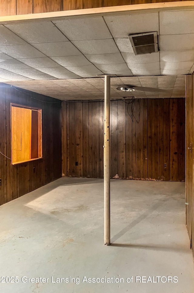 finished basement featuring a paneled ceiling and wood walls