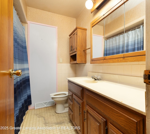 bathroom with visible vents, a wainscoted wall, toilet, tile walls, and vanity