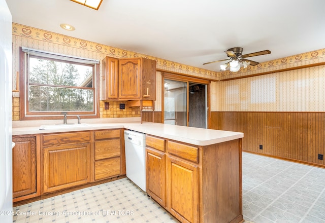 kitchen with light floors, a wainscoted wall, wallpapered walls, a sink, and dishwasher