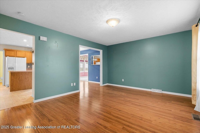 empty room with visible vents, a textured ceiling, light wood-type flooring, and baseboards