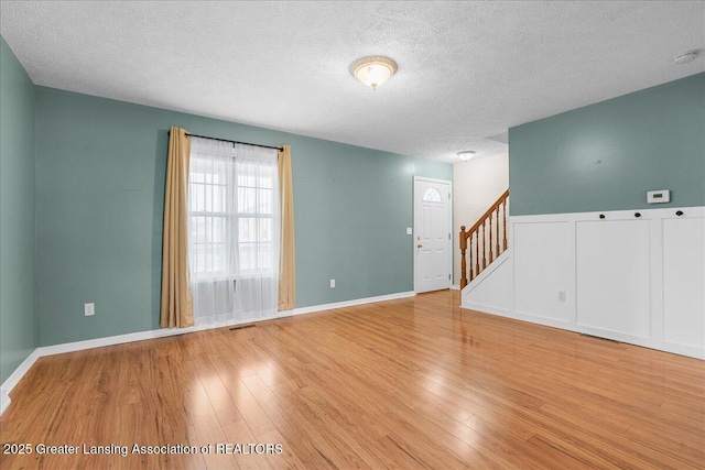 empty room featuring stairs, light wood-style floors, visible vents, and a textured ceiling