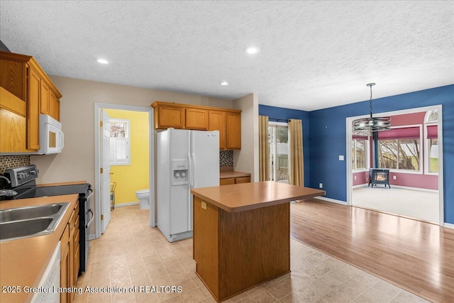 kitchen featuring a sink, a center island, white appliances, decorative backsplash, and light floors