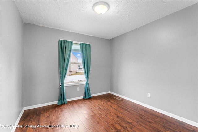 unfurnished room featuring baseboards, wood-type flooring, a textured ceiling, and visible vents