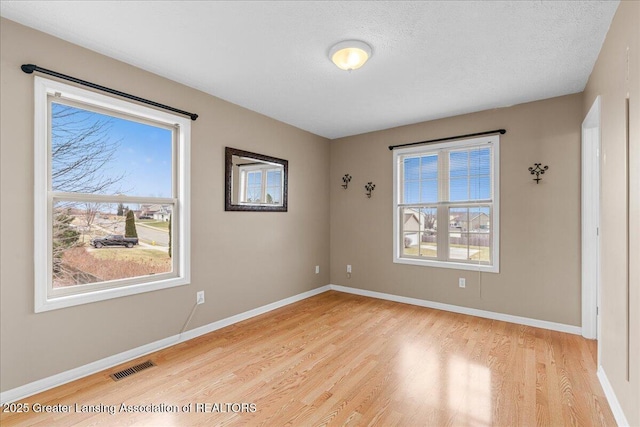 spare room featuring light wood finished floors, visible vents, a textured ceiling, and baseboards