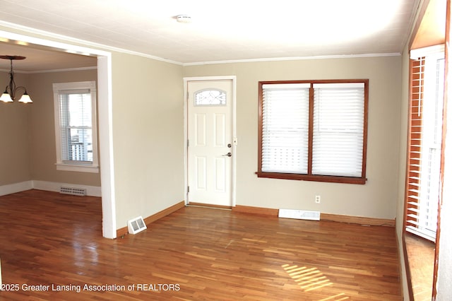 foyer with wood finished floors, visible vents, baseboards, crown molding, and a notable chandelier