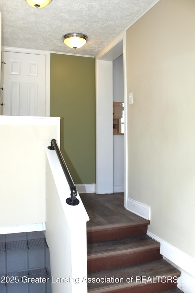 stairs featuring a textured ceiling, baseboards, and wood finished floors