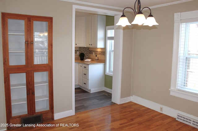 unfurnished dining area featuring a notable chandelier, wood finished floors, visible vents, and baseboards