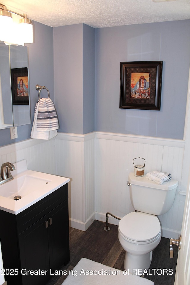 bathroom featuring a wainscoted wall, toilet, vanity, wood finished floors, and a textured ceiling