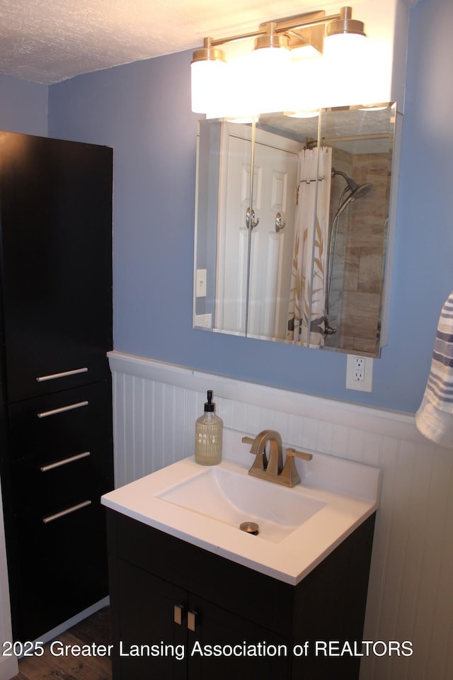 bathroom featuring a shower with curtain, vanity, a textured ceiling, and wainscoting