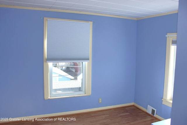 empty room featuring ornamental molding, wood finished floors, visible vents, and baseboards