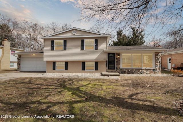 tri-level home with brick siding, a front yard, driveway, stone siding, and an attached garage