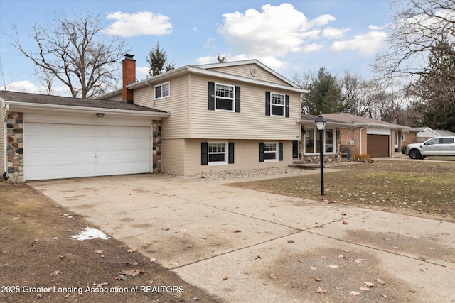 split level home featuring concrete driveway, brick siding, a garage, and a chimney