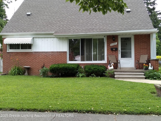 view of front facade with brick siding, a front lawn, and a shingled roof