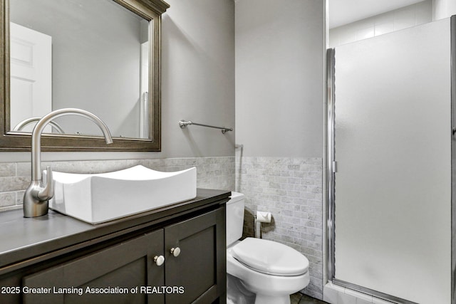 bathroom featuring vanity, a wainscoted wall, a stall shower, tile walls, and toilet