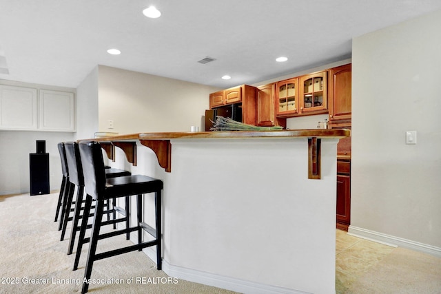 kitchen with visible vents, black fridge, a kitchen breakfast bar, and glass insert cabinets