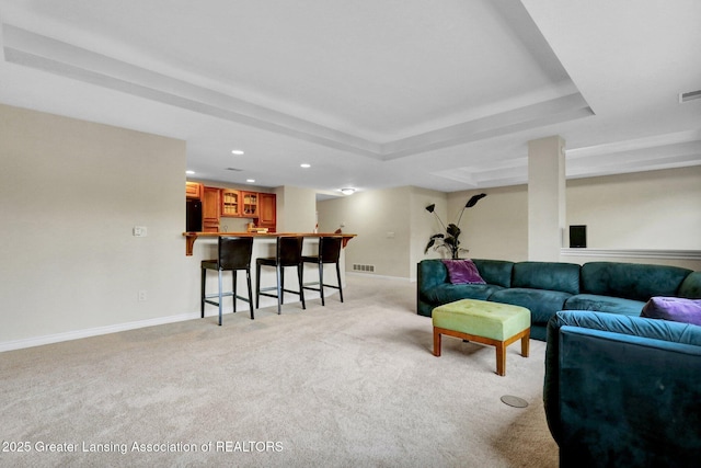 living area with visible vents, light carpet, a tray ceiling, indoor wet bar, and baseboards