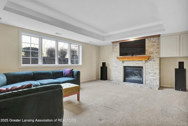 carpeted living area featuring visible vents, a fireplace, baseboards, and a tray ceiling