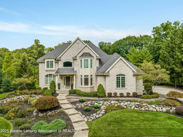 french country home featuring roof with shingles and a front lawn