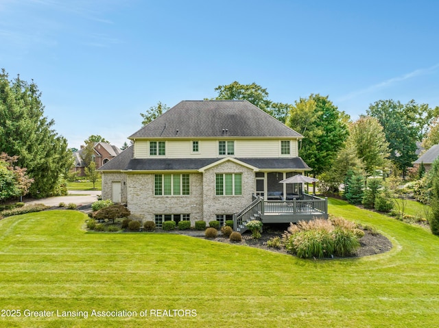 rear view of property with stone siding, a lawn, a deck, and a shingled roof