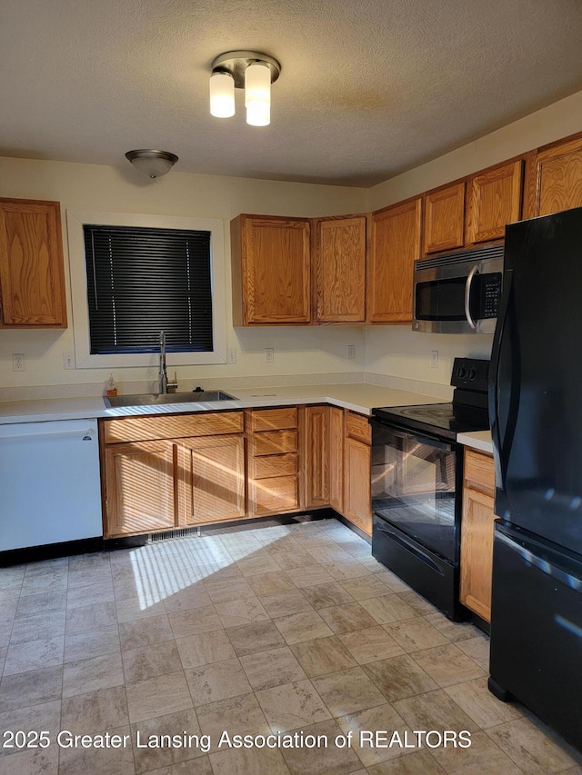 kitchen featuring black appliances, light countertops, brown cabinetry, a textured ceiling, and a sink