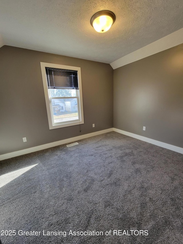 carpeted spare room with visible vents, a textured ceiling, baseboards, and vaulted ceiling