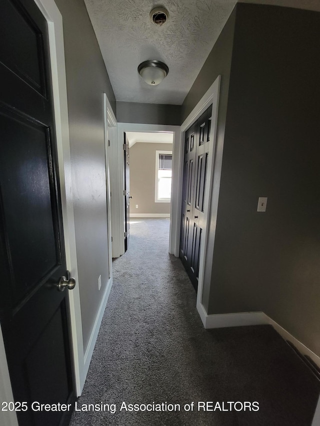 hall featuring baseboards, a textured ceiling, and carpet flooring