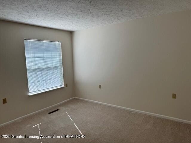 empty room featuring visible vents, a textured ceiling, and baseboards