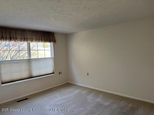 unfurnished room featuring baseboards, carpet floors, a textured ceiling, and visible vents