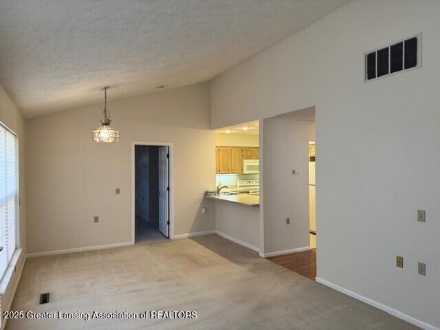 unfurnished living room with visible vents, lofted ceiling, a textured ceiling, and light colored carpet