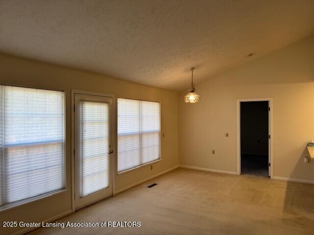 unfurnished dining area featuring visible vents, light carpet, a textured ceiling, and vaulted ceiling