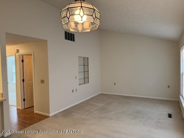 carpeted spare room with lofted ceiling, baseboards, and visible vents