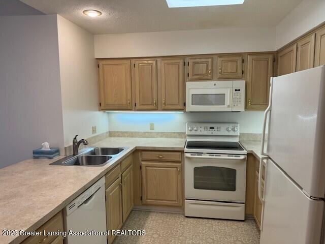 kitchen with white appliances, a skylight, light countertops, and a sink