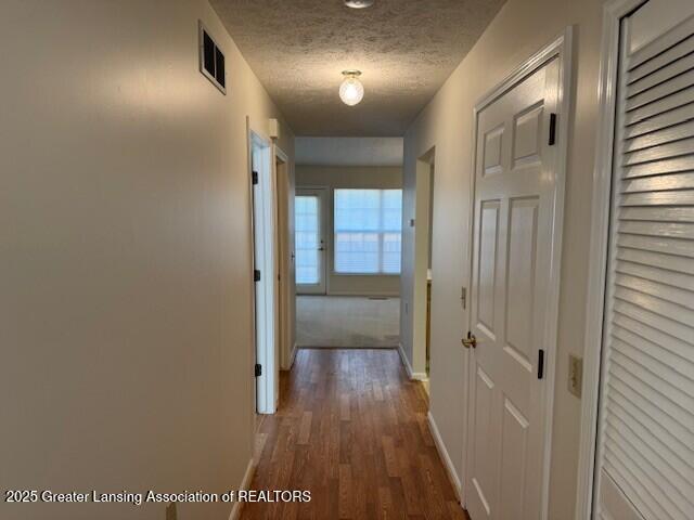 corridor featuring visible vents, a textured ceiling, baseboards, and dark wood-style flooring