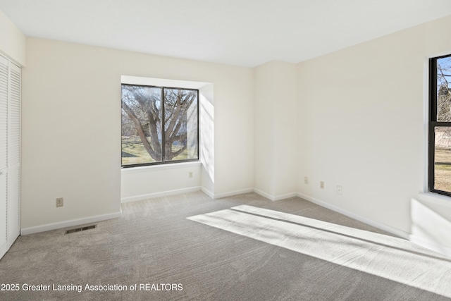 unfurnished bedroom featuring visible vents, multiple windows, carpet flooring, and baseboards