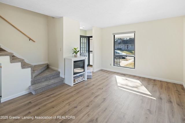 unfurnished living room featuring stairway, baseboards, and wood finished floors