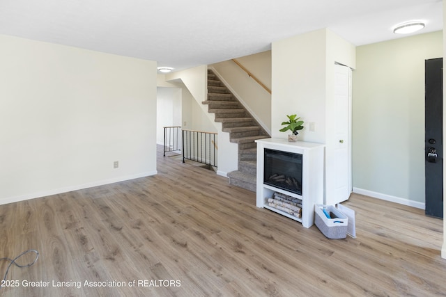 unfurnished living room featuring stairway, wood finished floors, and baseboards