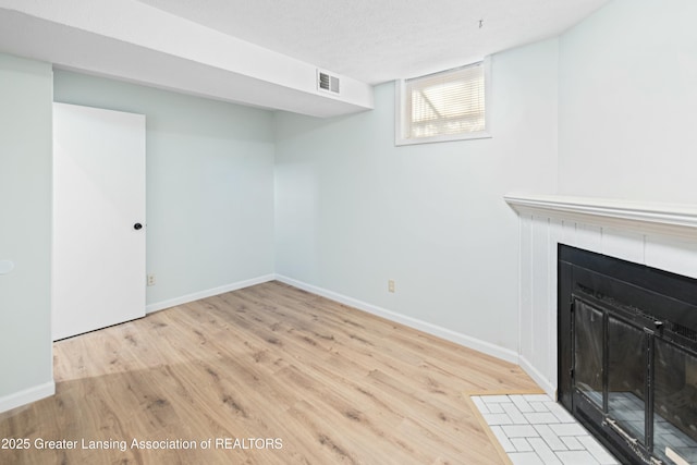 unfurnished living room featuring wood finished floors, visible vents, baseboards, a textured ceiling, and a tiled fireplace