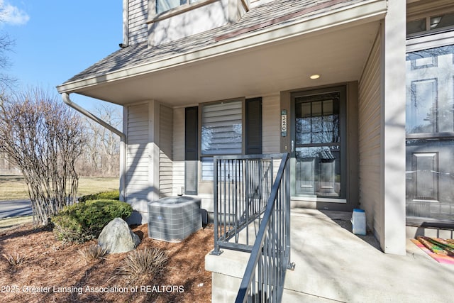 doorway to property with a porch, cooling unit, and a shingled roof