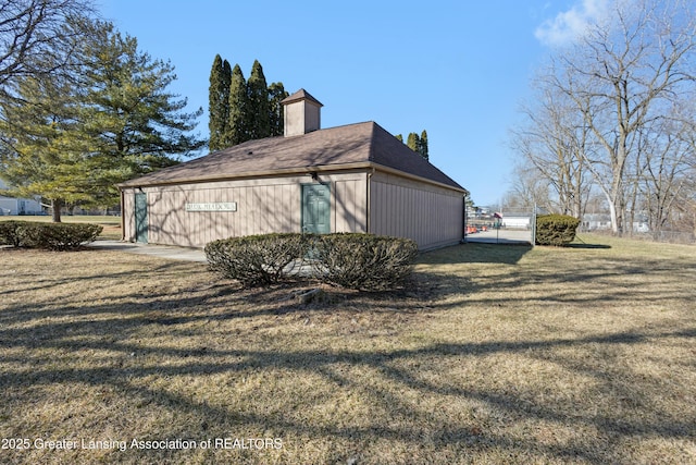 view of side of property with a shingled roof, a lawn, a chimney, and a gate