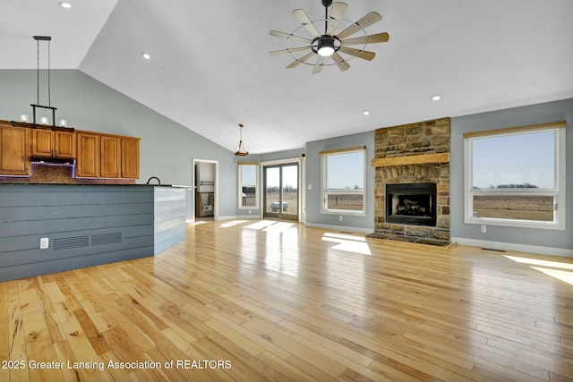 unfurnished living room with visible vents, light wood-style flooring, a fireplace, high vaulted ceiling, and a ceiling fan