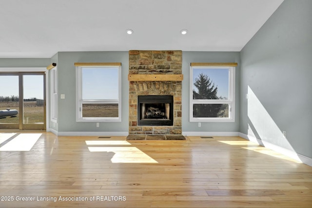 unfurnished living room featuring baseboards, wood-type flooring, a stone fireplace, and visible vents