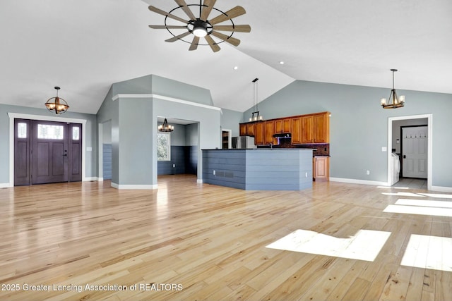 unfurnished living room with ceiling fan with notable chandelier, high vaulted ceiling, light wood-type flooring, and baseboards