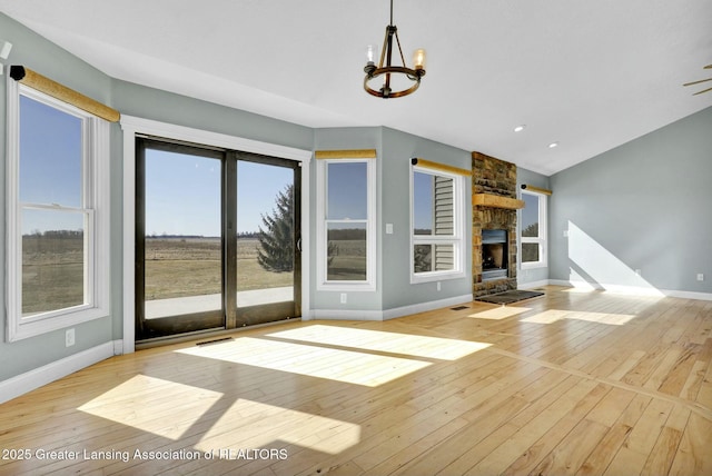 unfurnished living room featuring visible vents, baseboards, a chandelier, a stone fireplace, and wood-type flooring