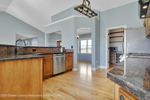 kitchen featuring brown cabinetry, dark stone counters, vaulted ceiling, appliances with stainless steel finishes, and light wood-type flooring