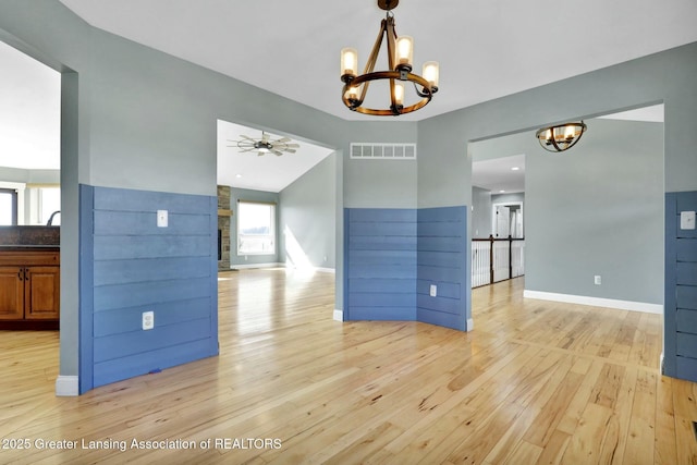 spare room with visible vents, baseboards, light wood-type flooring, lofted ceiling, and ceiling fan with notable chandelier