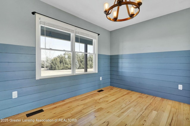 spare room with wooden walls, a notable chandelier, wood finished floors, and visible vents