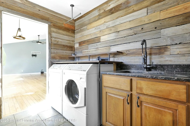 clothes washing area with washing machine and clothes dryer, wooden walls, visible vents, cabinet space, and a sink